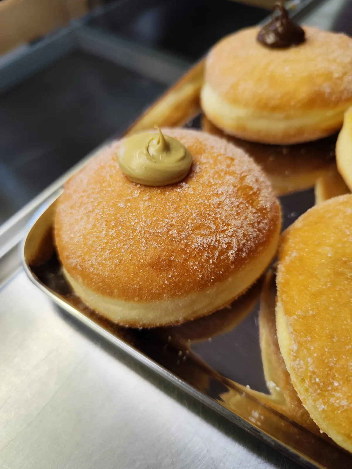 Bomboloni passati nello zucchero, con un ciuffo di crema sulla sommità, su una teglia d'acciaio.