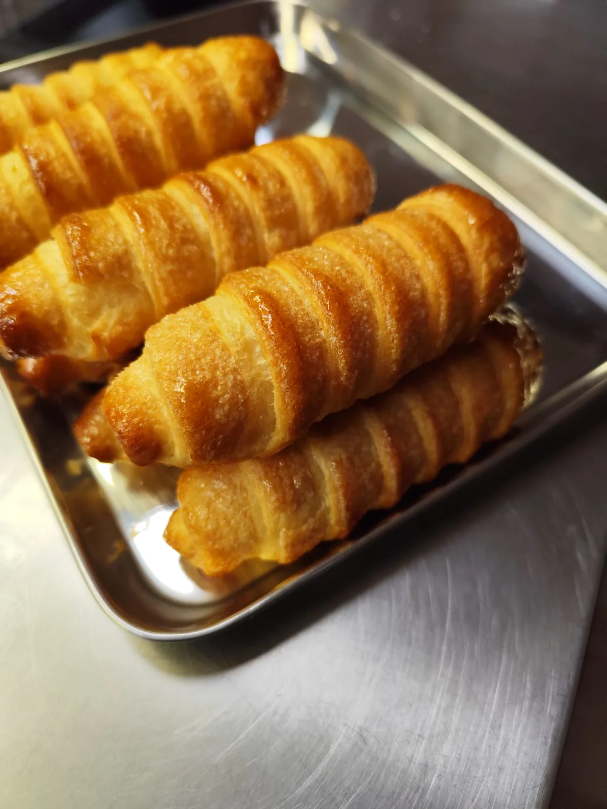 Cannoncini di pasta sfoglia dorati, ancora da farcire, impilati in una vaschetta d'acciaio.