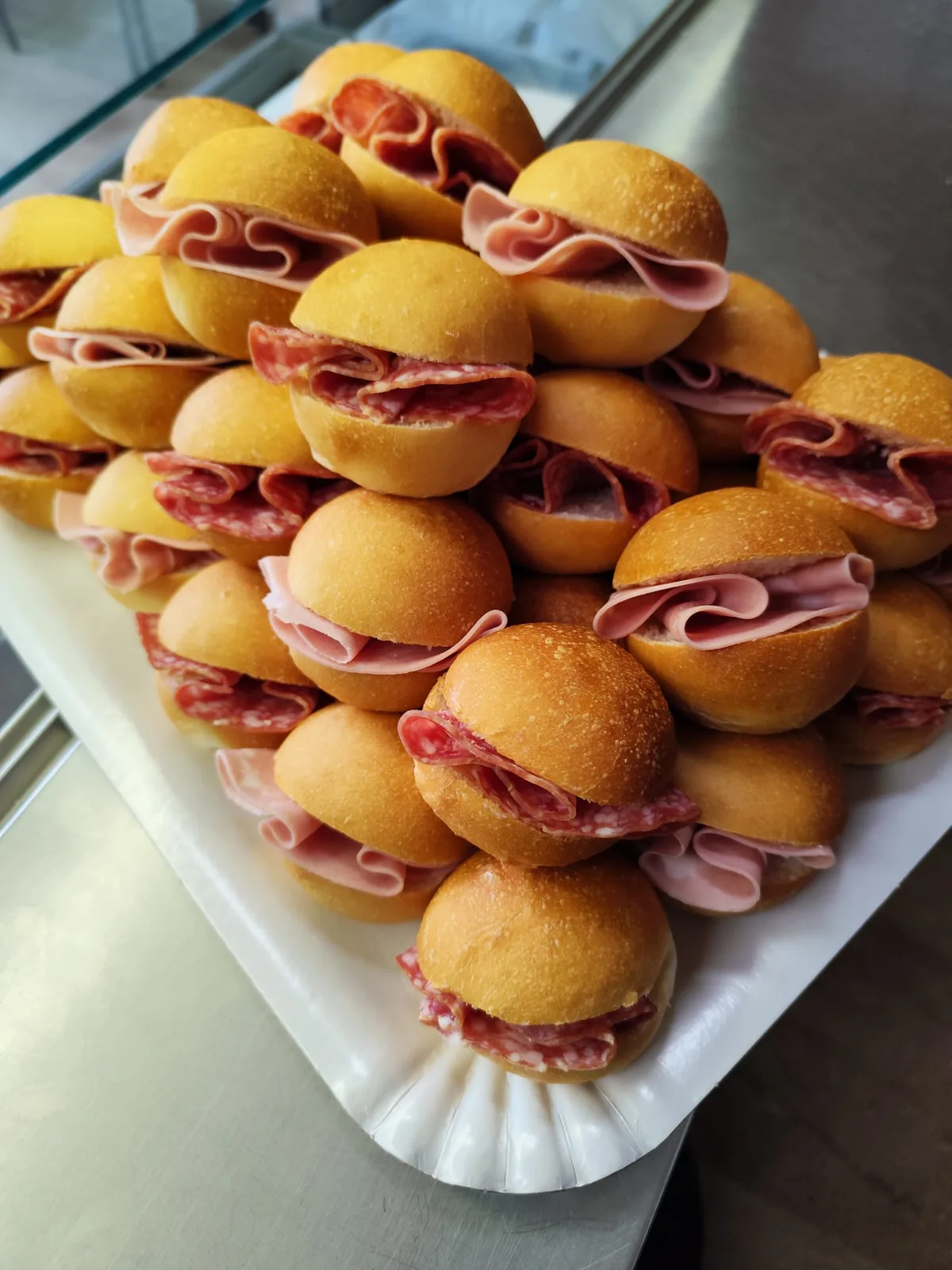 Piramide di panini mignon farciti con prosciutto cotto e salame, su un vassoio da buffet.