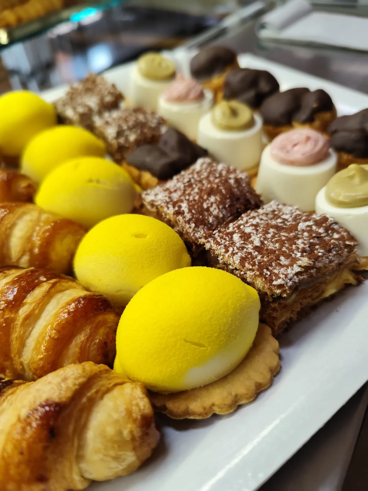 Vassoio di pasticceria mignon: monoporzioni gialle al limone, millefoglie, bignè al cioccolato e piccoli dolci alla crema.